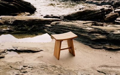 A slatted top teak wood stool placed on a beach